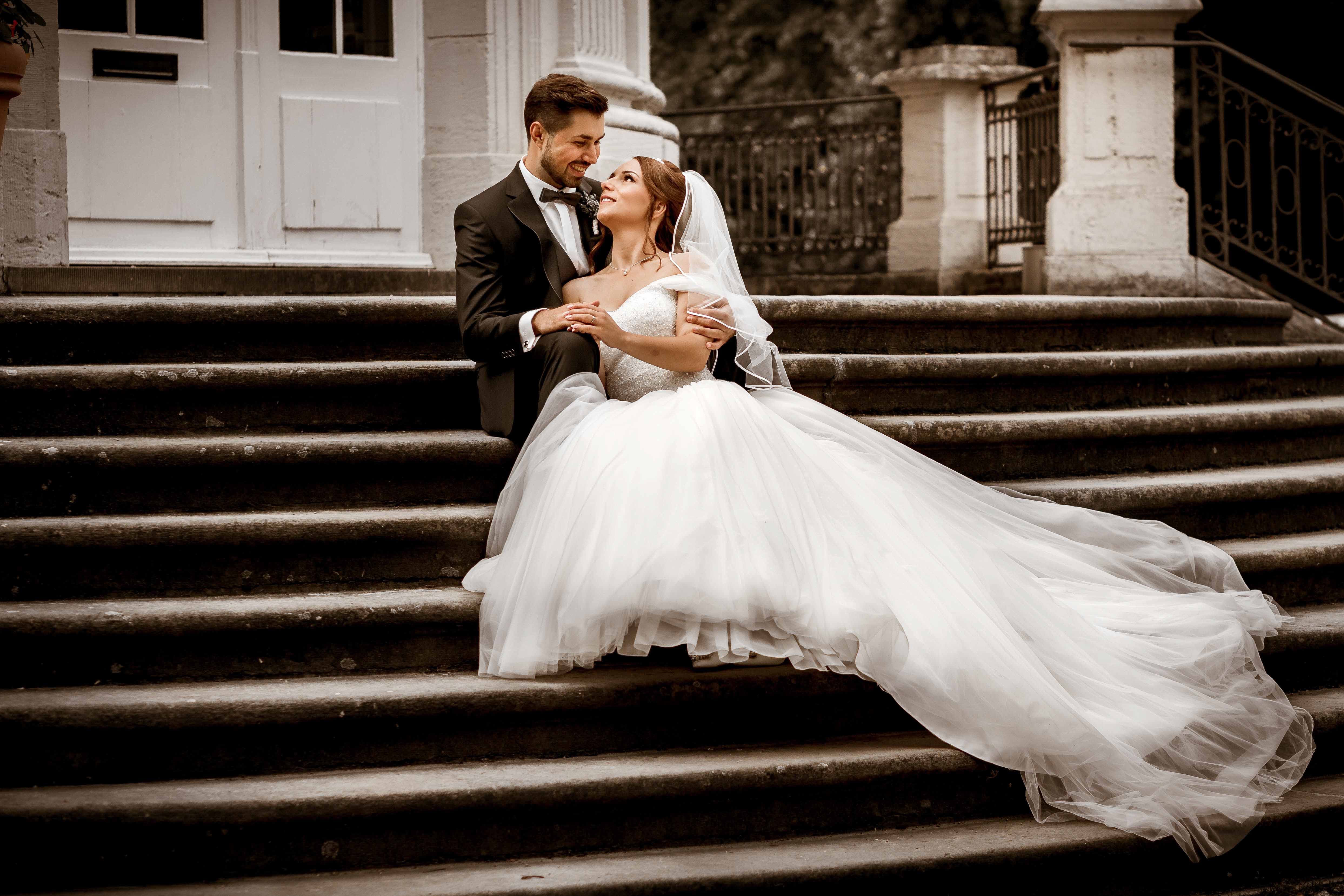 Hochzeitspaar sitzt auf Treppe und Braut liegt im Arm des Bräutigam